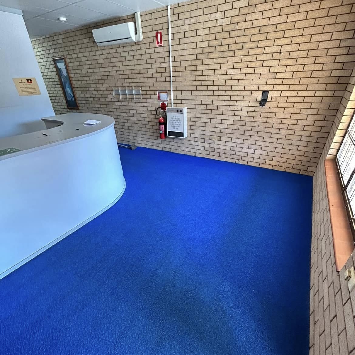 Office reception with bright blue carpet, curved white desk and brick wall